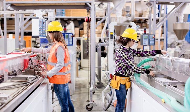 2 women in hard hats attending machines in manufacturing plant