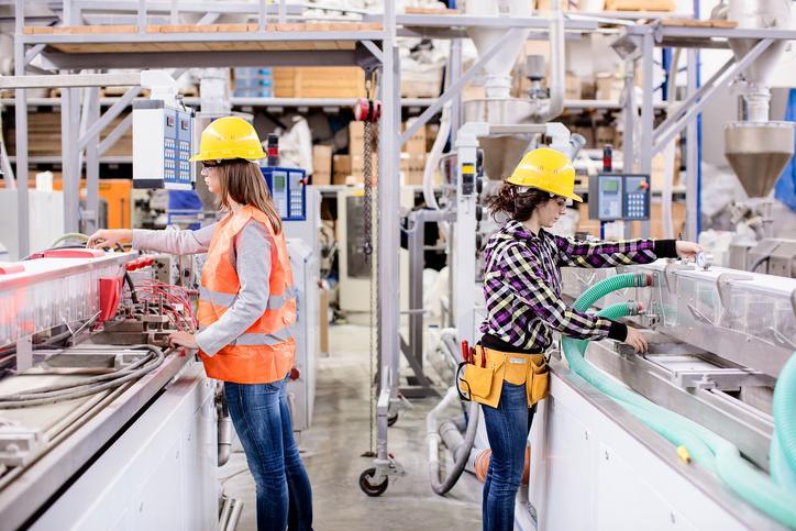 2 women in hard hats attending machines in manufacturing plant