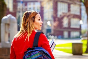 Woman wearing backpack and carrying a stack of textbooks.