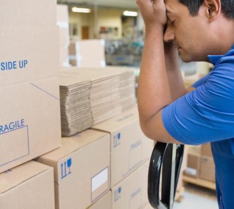 sleepy man resting his head in his hands as he stands beside a stack of boxes in a warehouse