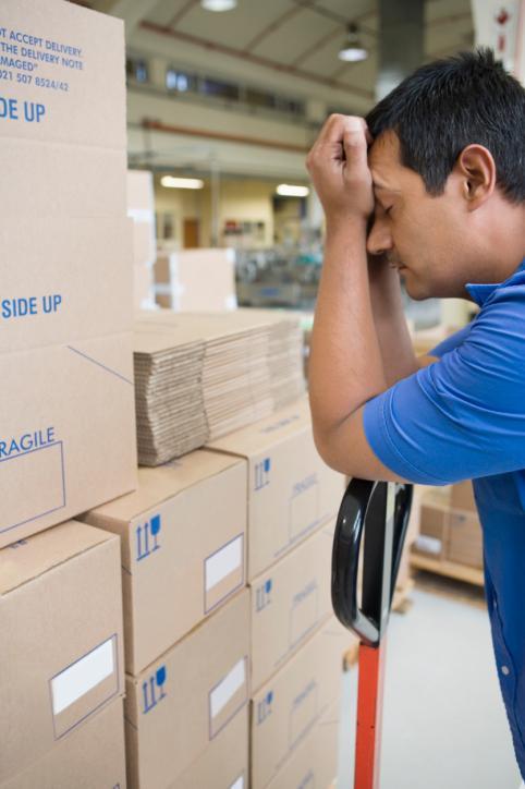 sleepy man resting his head in his hands as he stands beside a stack of boxes in a warehouse