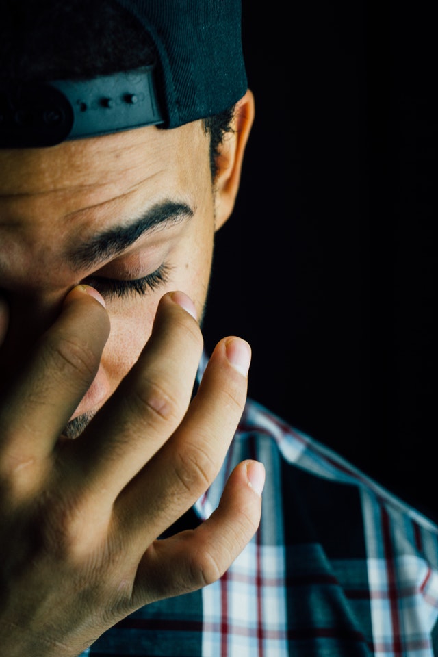 Man wearing baseball cap rubbing his eye with his finger