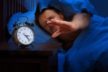 sleepy man in bed reaches for his alarm clock