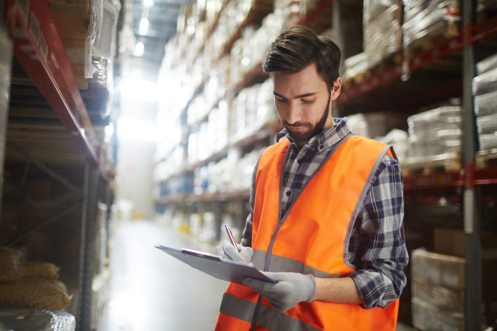 man in reflective vest writing on a clipboard in a warehouse