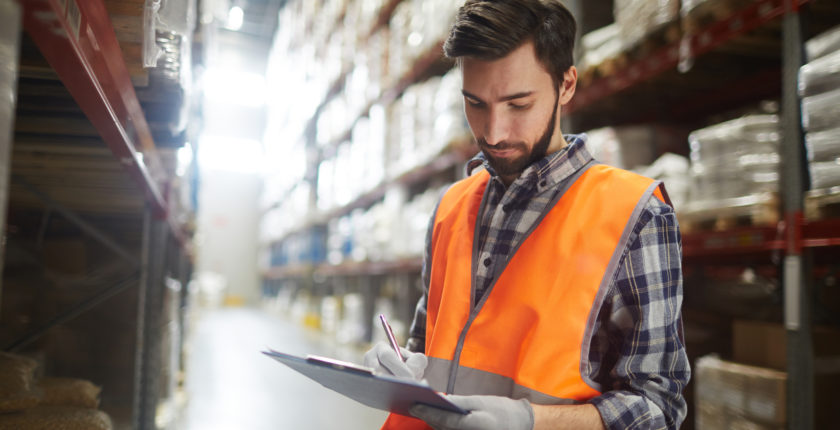 man in reflective vest writing on a clipboard in a warehouse