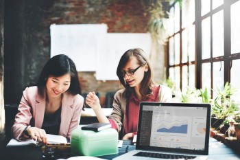 2 woman sitting beside each other with an open laptop