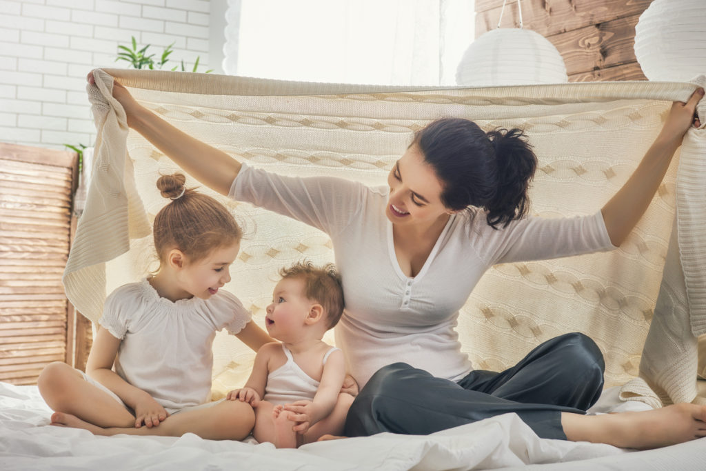 Woman with 2 yojng children playing under a blanket