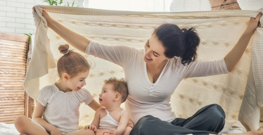 Woman with 2 yojng children playing under a blanket