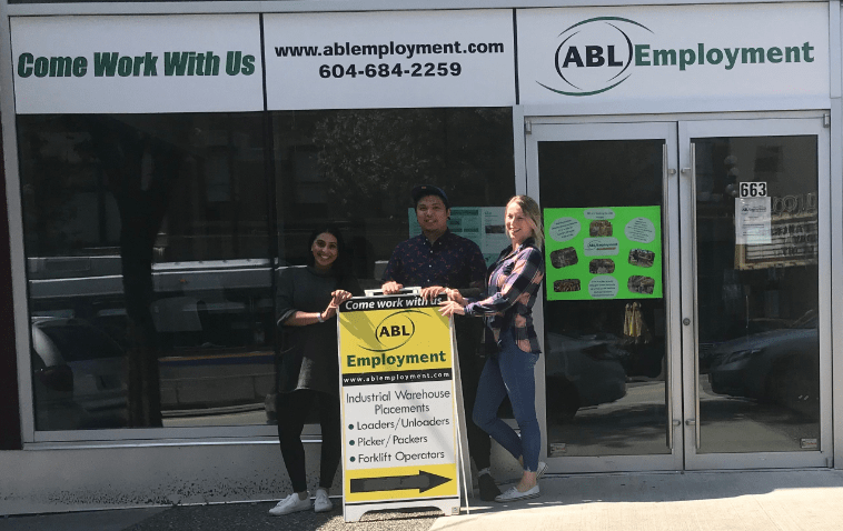 Staff members posing outside exterior of office space with sandwich board sign