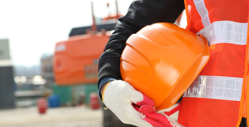 person in reflective PPE holding a hard hat outside