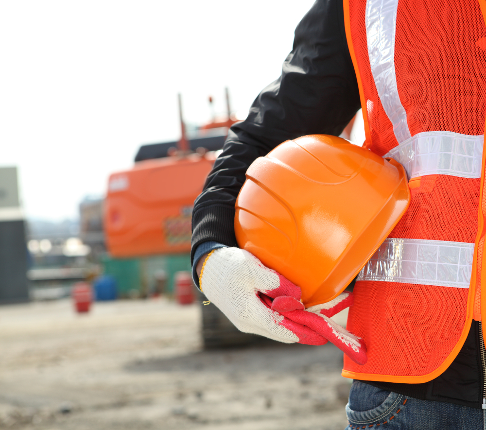 person in reflective PPE holding a hard hat outside