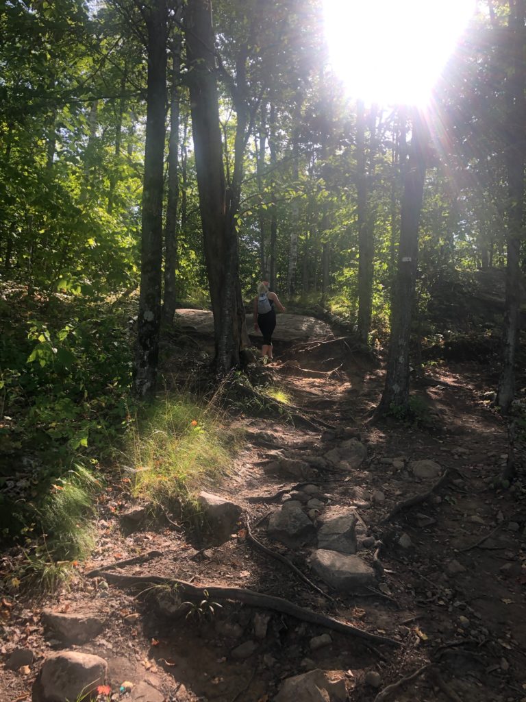 Woman hiking on a wooded trail in the dappled sunlight