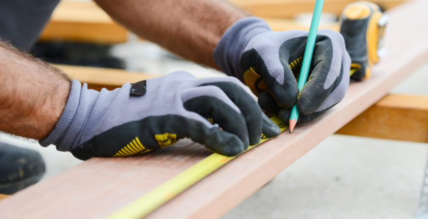 close up detail of manual worker hands working with a measuring tape and pencil in wood plank