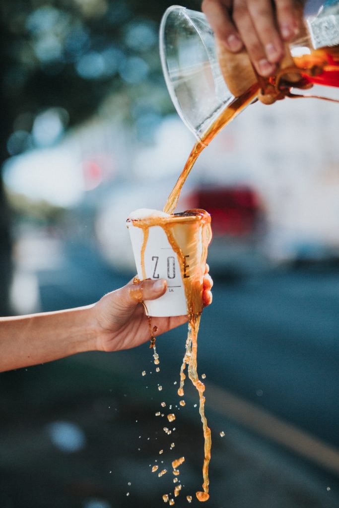 coffee being poured into a paper cup and overflowing