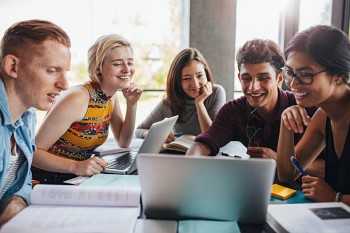 multi-ethnic gathering of young people around 2 laptops at a meeting table