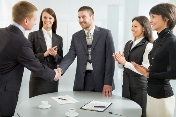 5 people gathered around a round table, some clapping, some shaking hands.