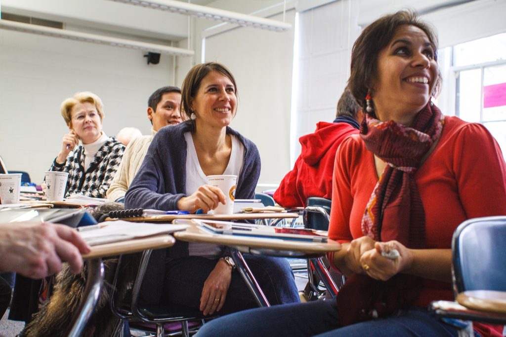 adult students smiling while huddled grouped together at desks