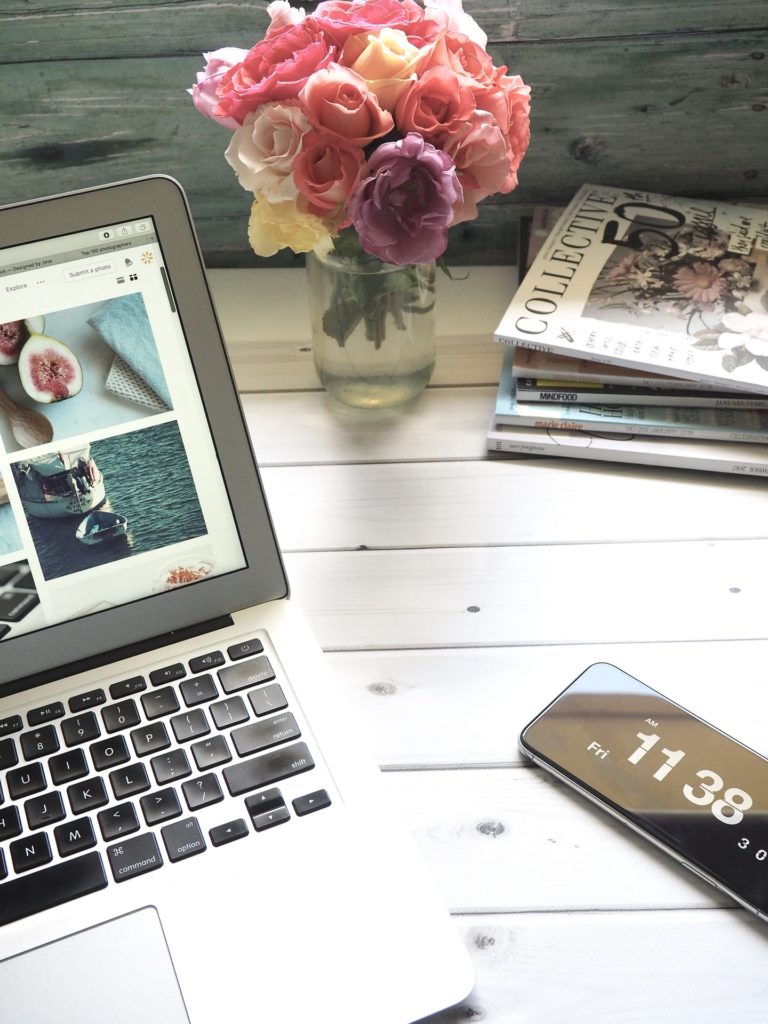 a casual home office desk with roses in a vase, magazines, laptop, and cell phone.