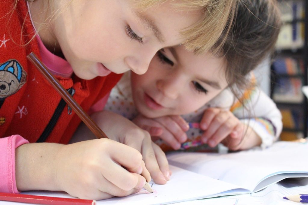 two toddlers leaning over a colouring book with their heads together.