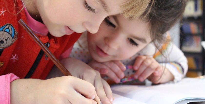 two toddlers leaning over a colouring book with their heads together.