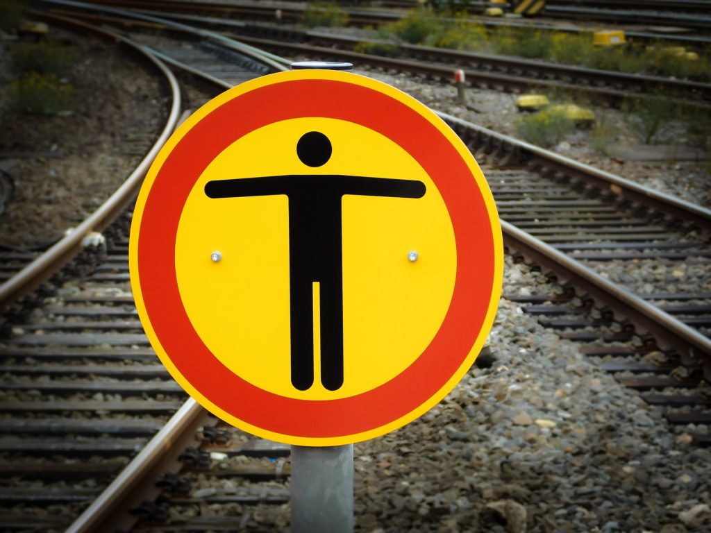 railway tracks converging and a yellow and red warning sign