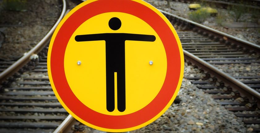 railway tracks converging and a yellow and red warning sign