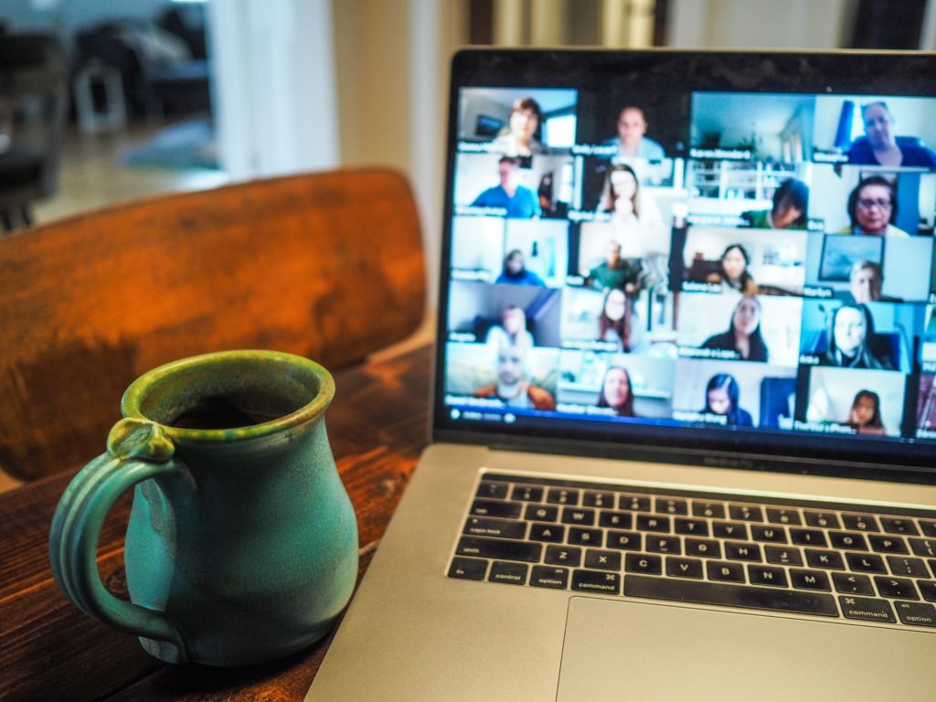 laptop displaying virtual meeting participants with coffee mug beside it