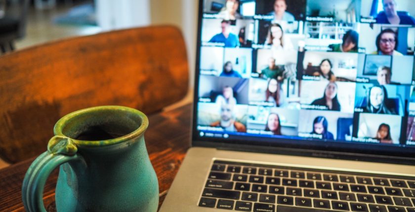 laptop displaying virtual meeting participants with coffee mug beside it