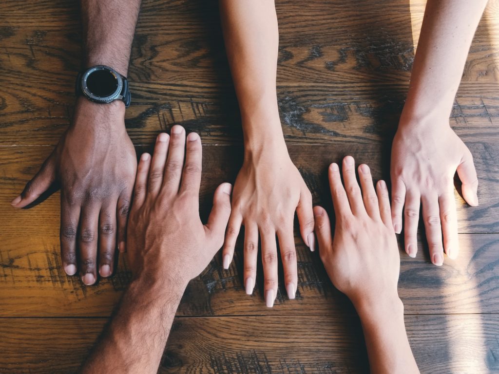 multiple hands of people with different skin tones resting on a tabletop