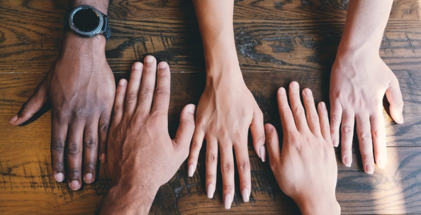 multiple hands of people with different skin tones resting on a tabletop