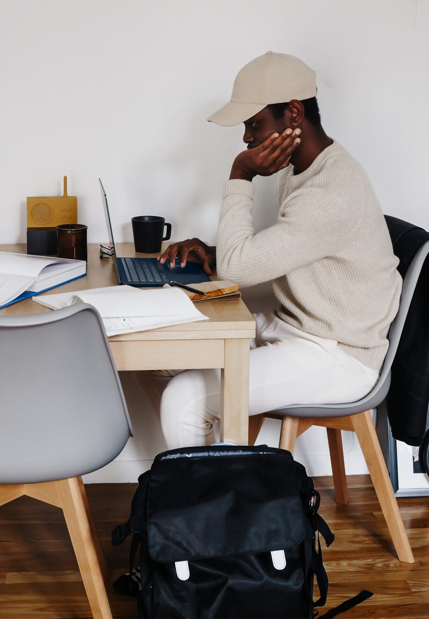 man wearing baseball cap sitting at desk with laptop