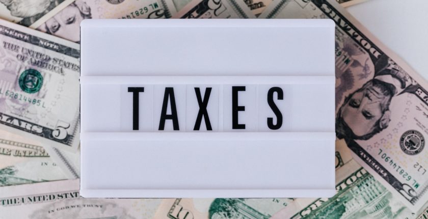 word "taxes" on a white sign, resting on a bed of banknotes