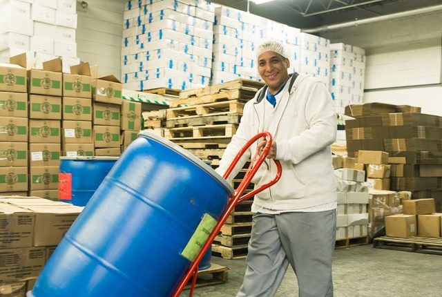 man wearing workclothes and using handcart to move a big plastic barrel