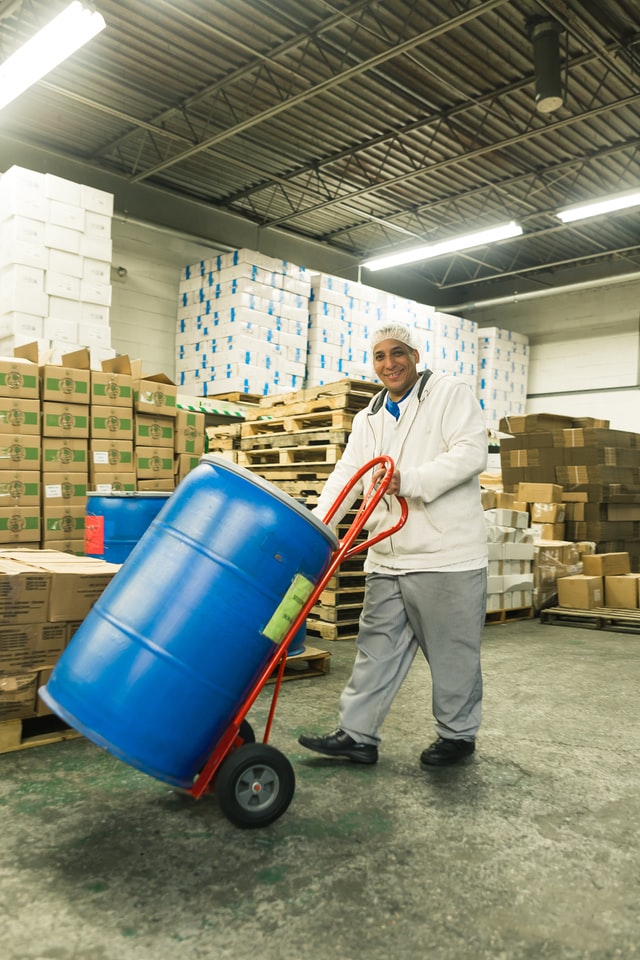 man wearing workclothes and using handcart to move a big plastic barrel