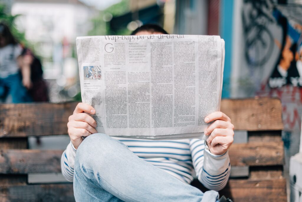 person reading newspaper on park bench