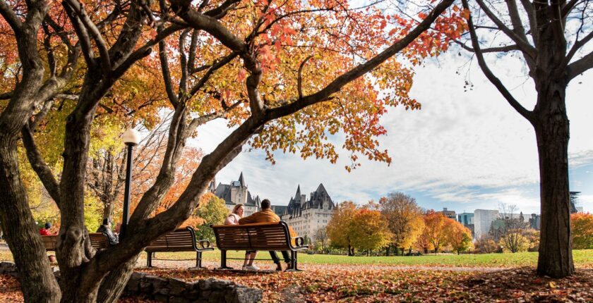 2 people sit on a park bench with Canadian parliament building in background