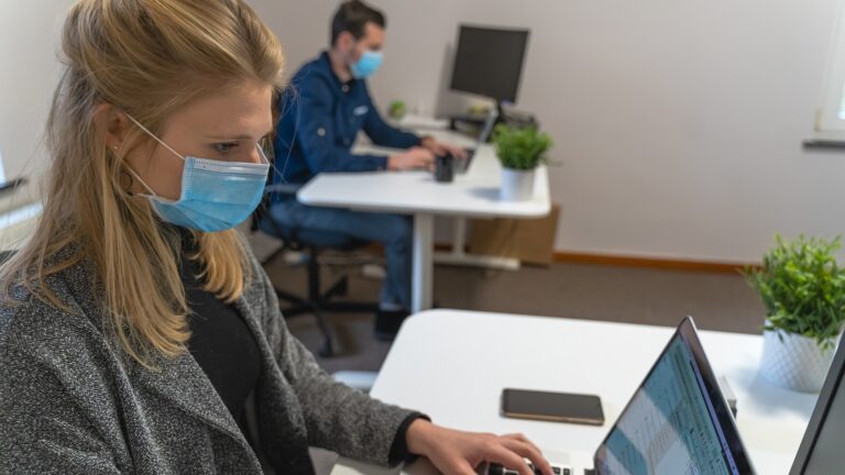 man and woman work at separate desks - returning to the office