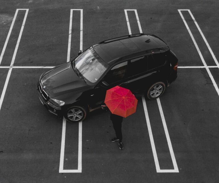 car in parking lot beside person carrying red umbrella