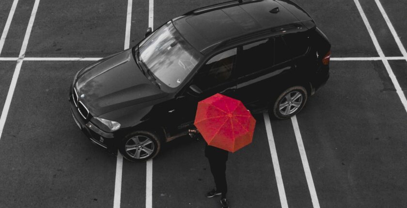 car in parking lot beside person carrying red umbrella