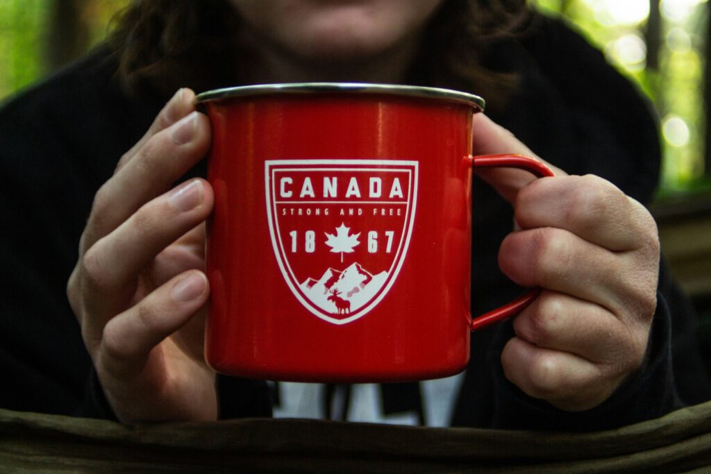 Person outdoors holding a red tin mug with Canada graphic.