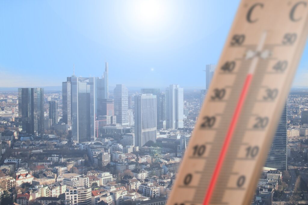 A city under a sunny sky in the background of the image, with a thermometre in the foreground