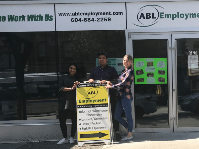 Staff members posing outside exterior of office space with sandwich board sign